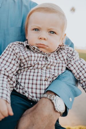 A baby in a checkered shirt gazes at the camera with bright blue eyes.