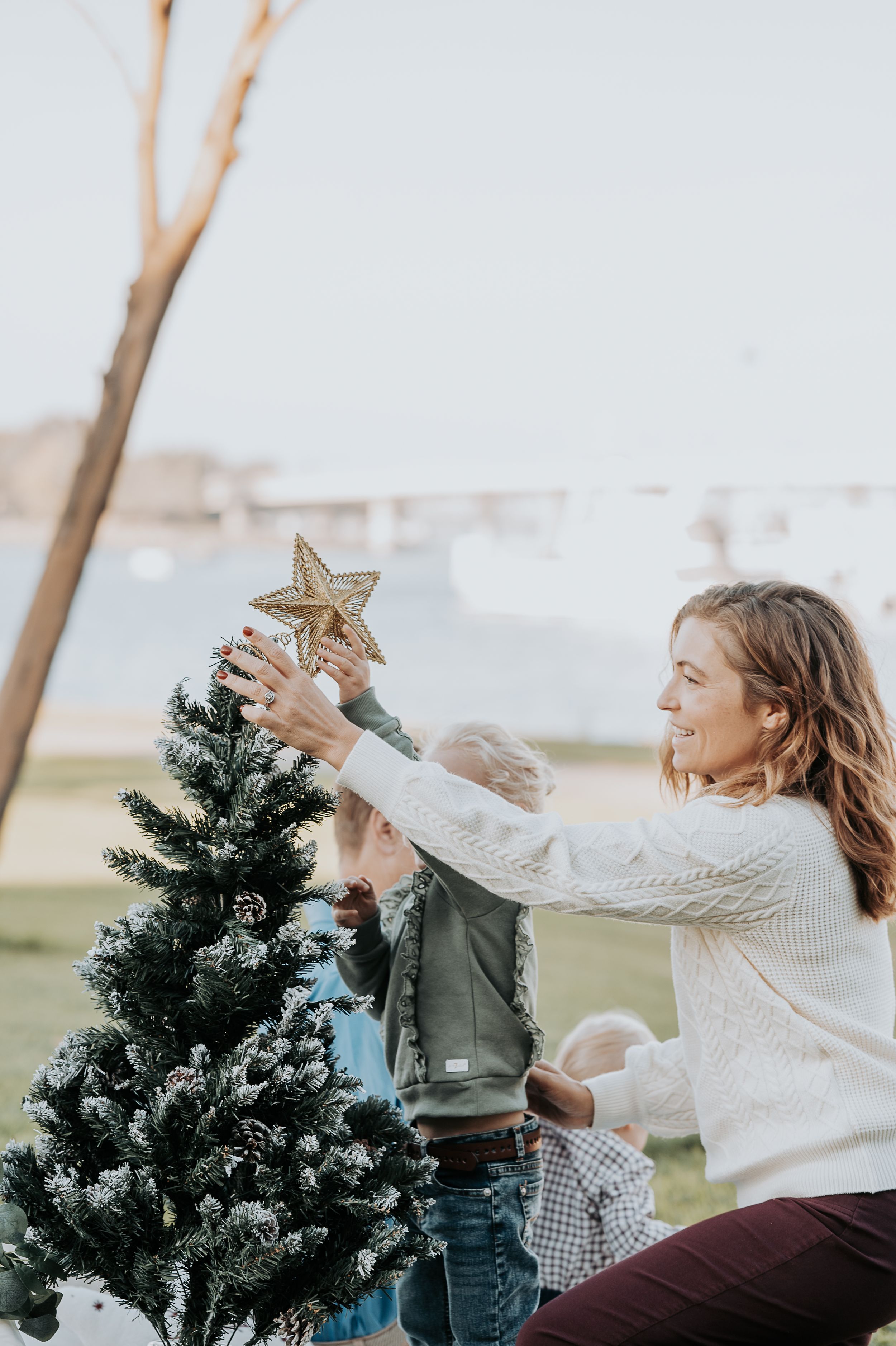 Mother helping child place star on top of outdoor Christmas tree.