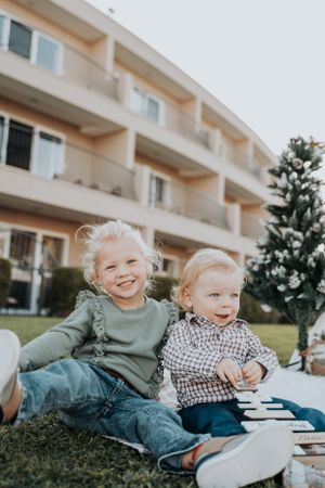 Two children sitting together and laughing outside a residential building.