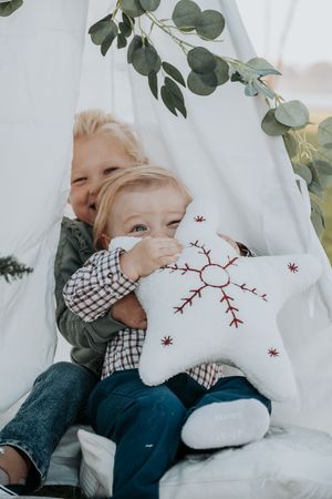 Child holding a decorative white pillow with red embroidery against white backdrop.