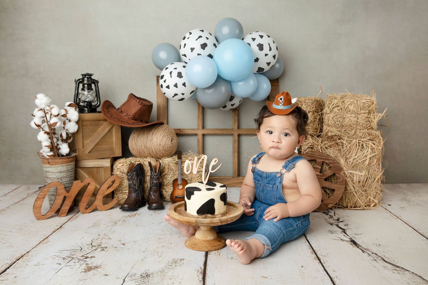 Rustic first birthday scene with blue balloons, hay bales and wooden decorations.