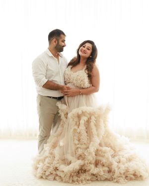 Couple sharing joyful moment in cream formal wear against white background.