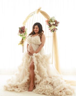 Maternity portrait under floral arch in ruffled cream gown.