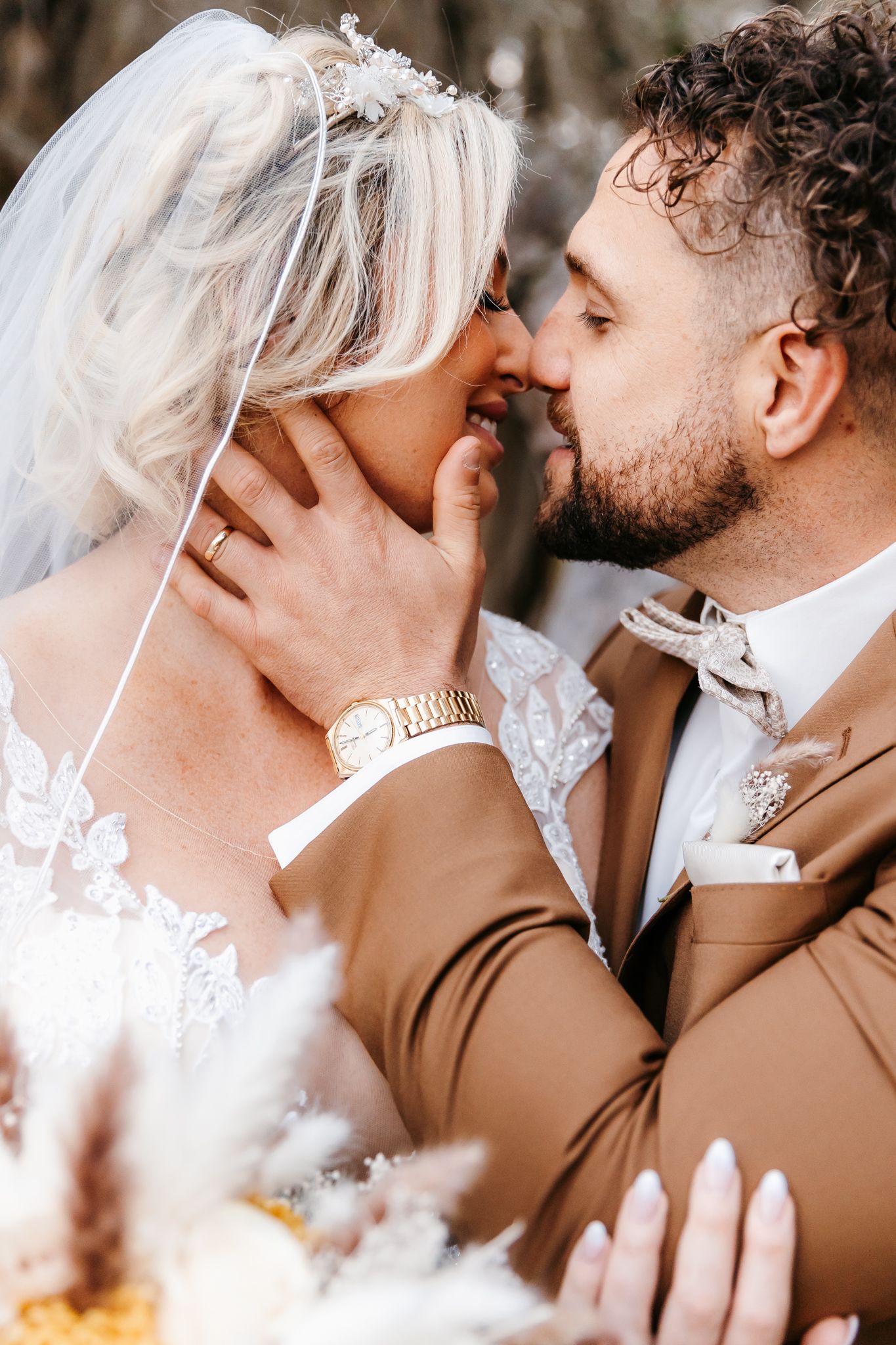 Bride and groom sharing an intimate moment, nearly kissing, with floral bouquet in foreground.