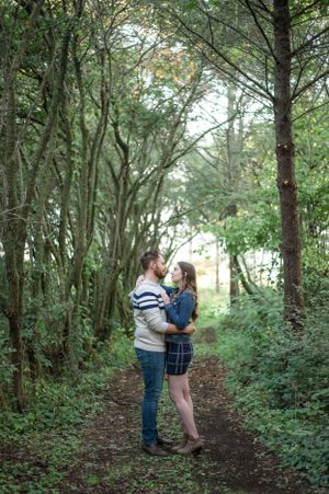 A romantic couple embraces on a tree-lined nature path surrounded by lush greenery.
