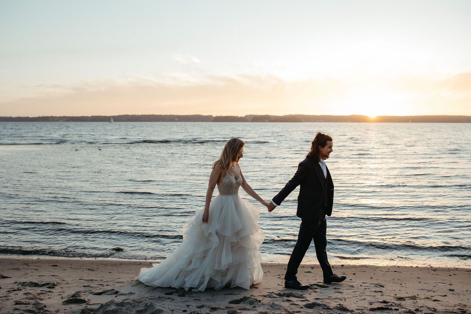 Romantic beach wedding photoshoot showing couple walking along shoreline at sunset.
