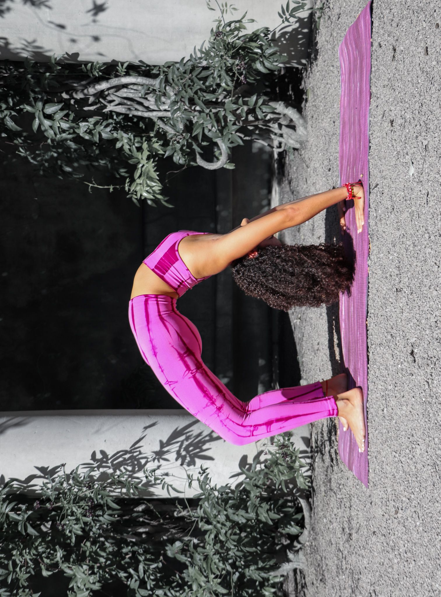 Advanced yoga backbend pose in vibrant pink activewear against concrete wall.
