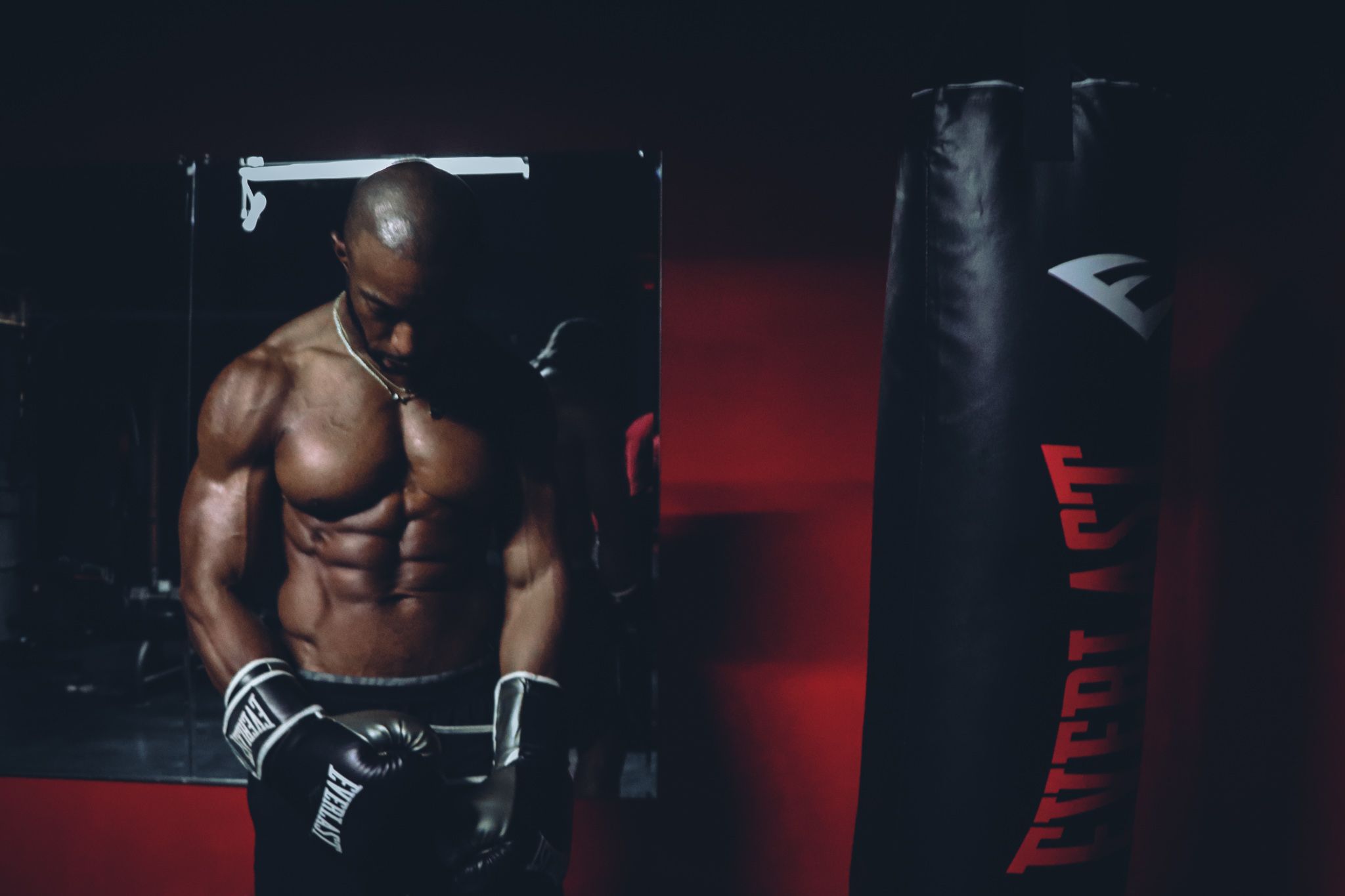 Muscular athlete training with boxing equipment in dimly lit gym environment.
