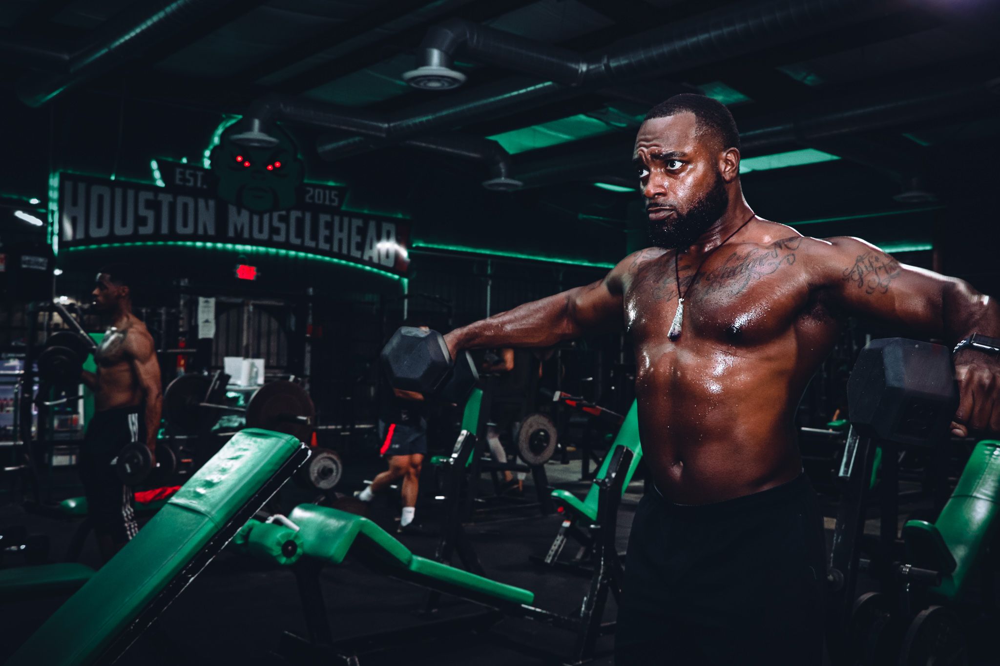 Bodybuilder working out in gym with neon green lighting and exercise machines visible.
