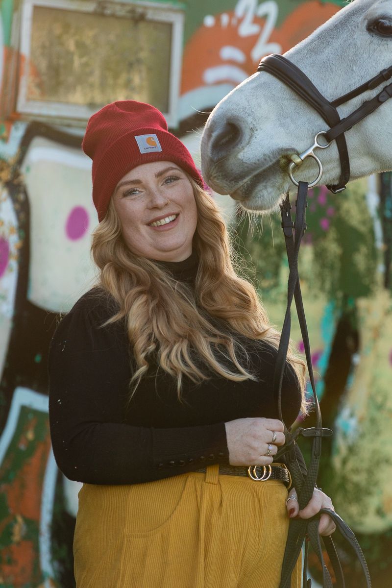 A cheerful moment between a white horse and someone wearing a red beanie against colorful street art.