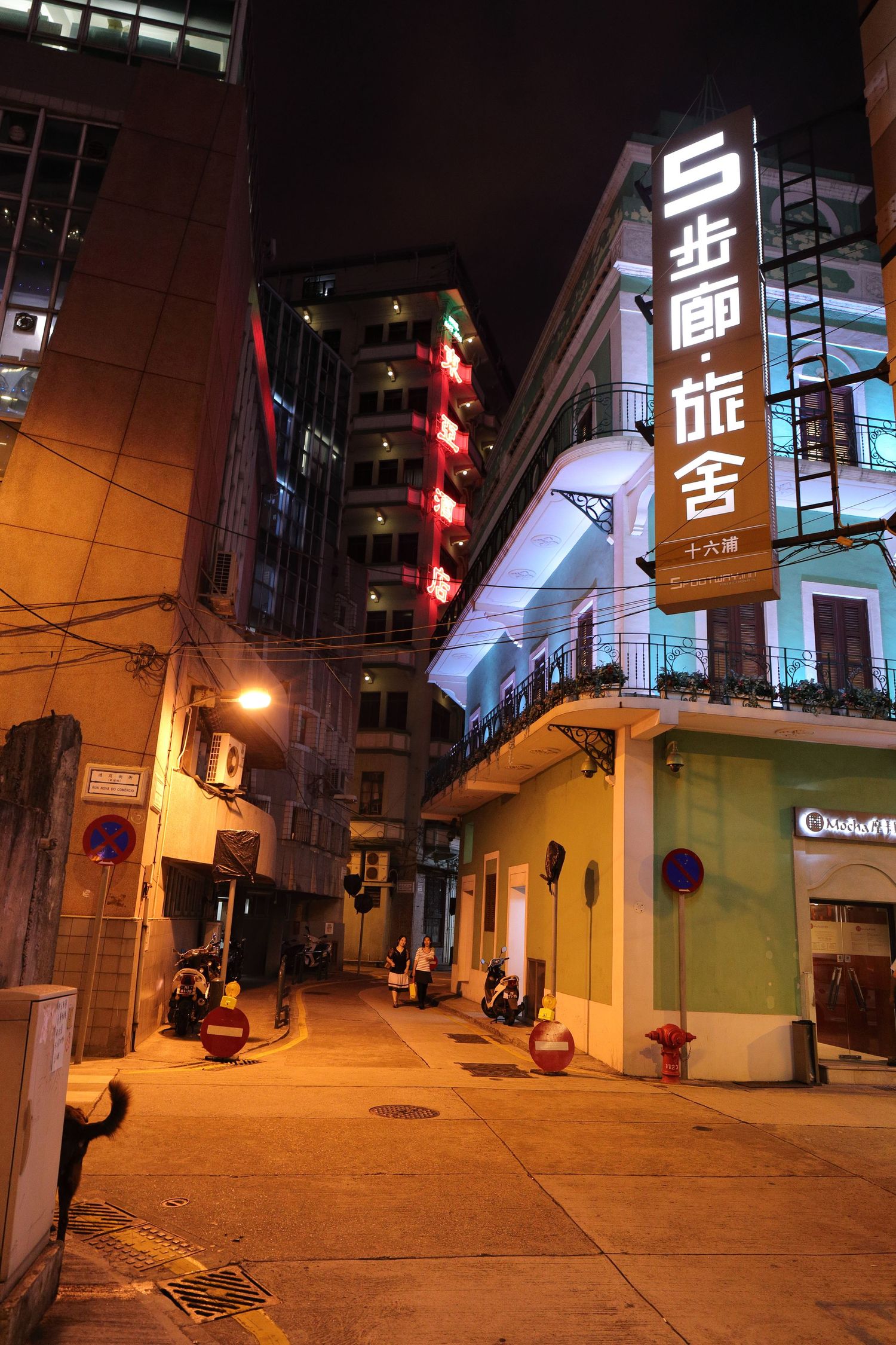 Nighttime street scene in Asia with glowing neon signs and yellow buildings.