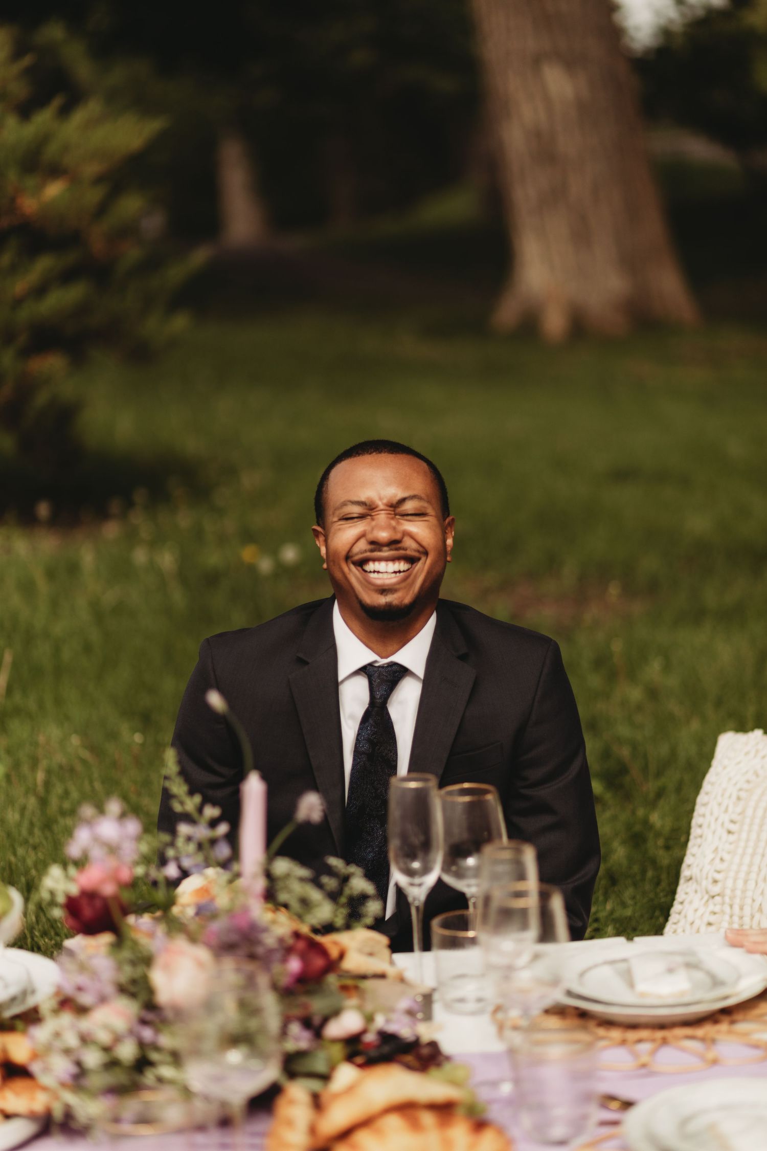 A joyful moment captured at an elegant outdoor wedding reception with wine glasses and floral arrangements on the table.