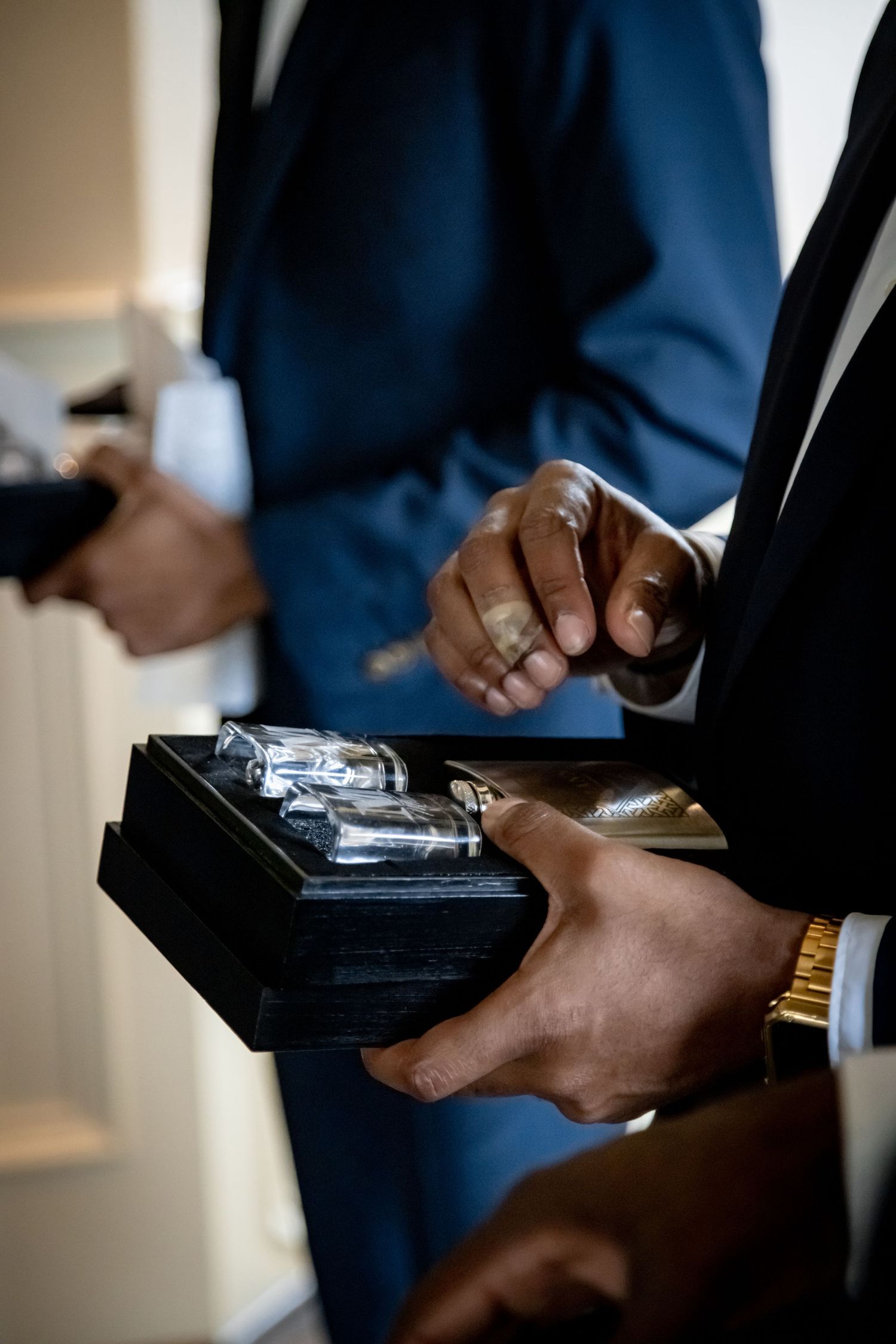 Close-up of hands handling wedding rings in an elegant black presentation box.