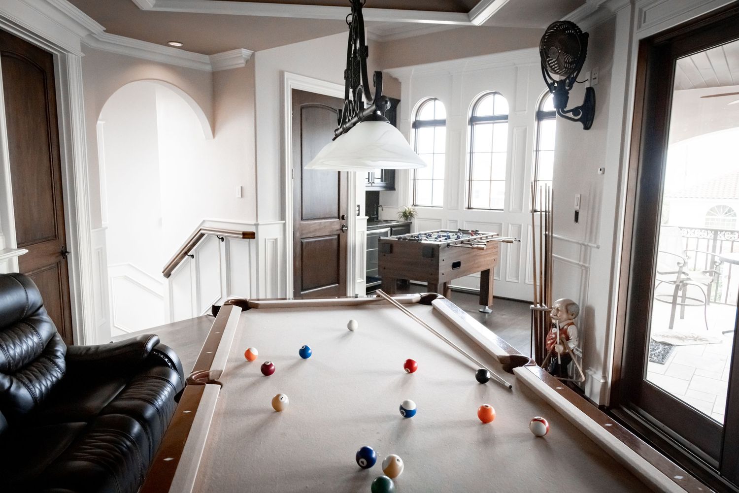 Modern game room with pool table, leather seating, and large arched windows overlooking scenic views.