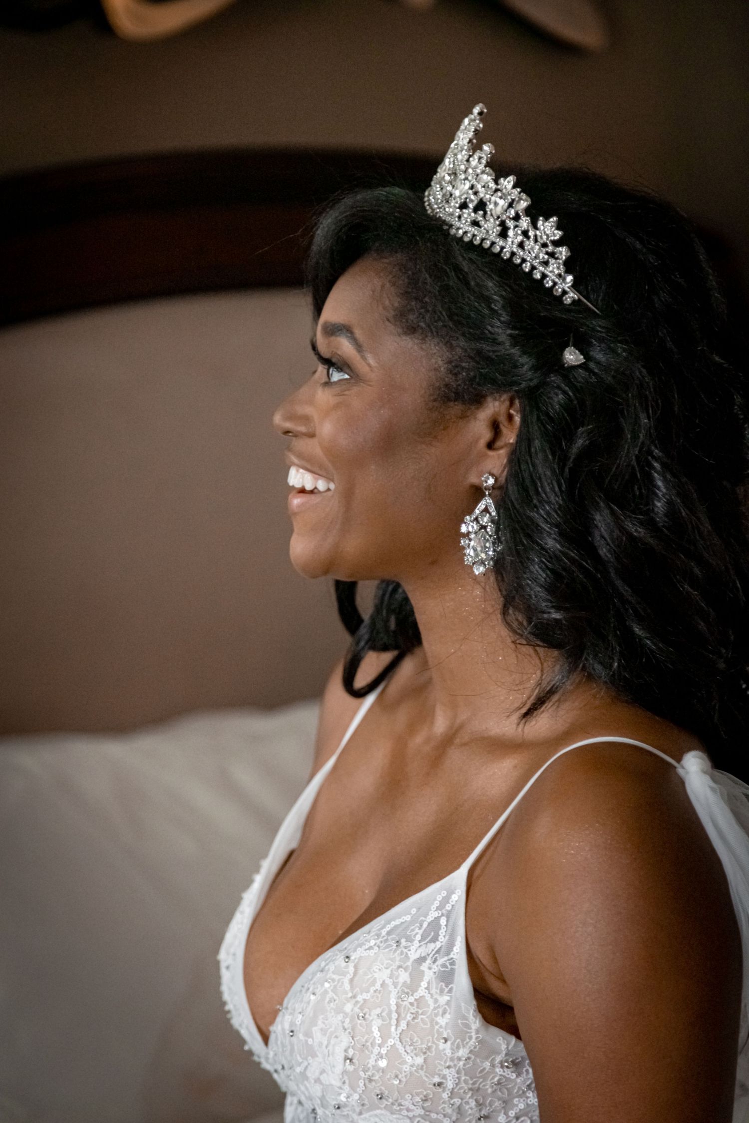 Bride wearing sparkling tiara and diamond earrings smiles radiantly in profile.