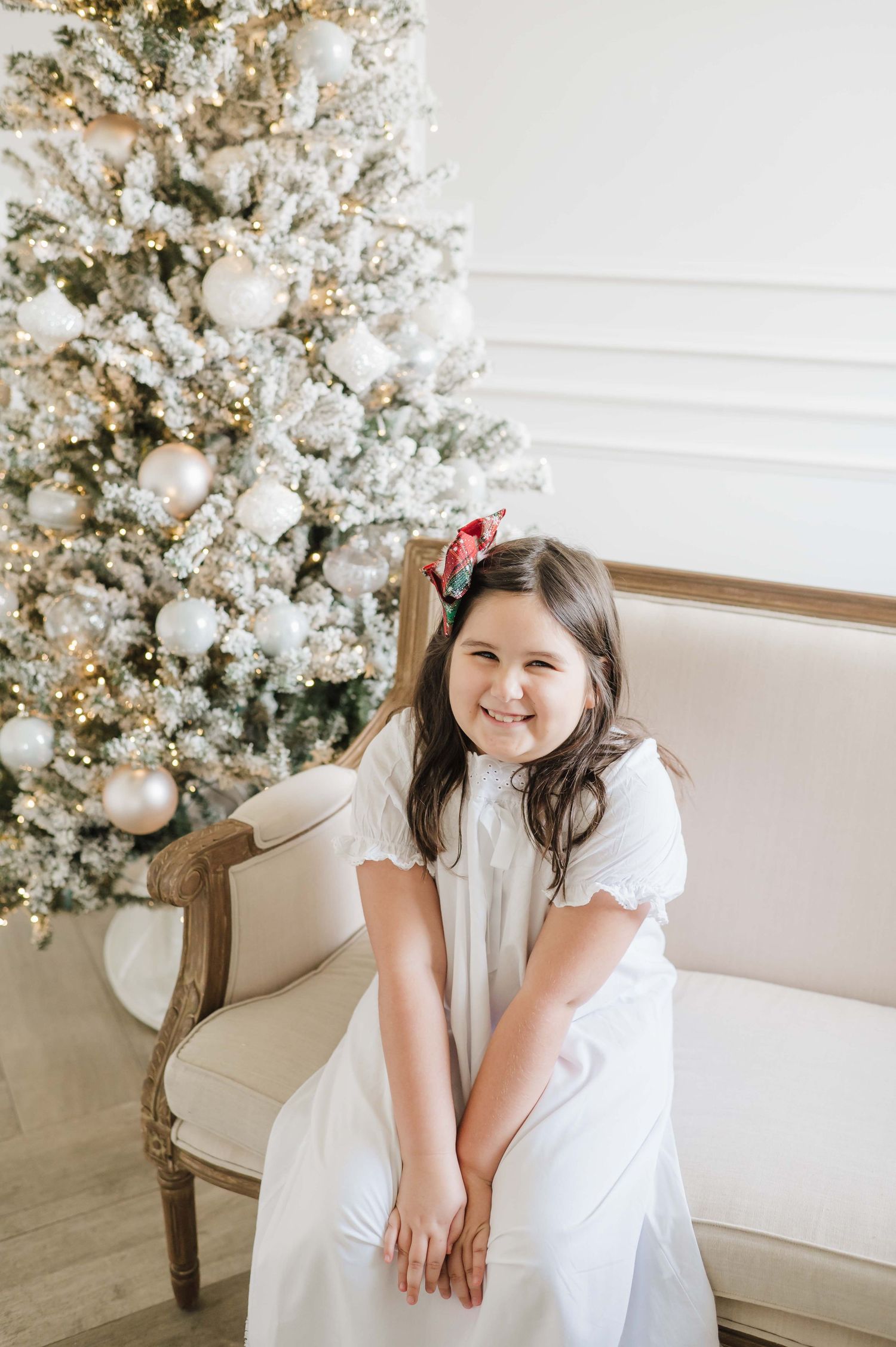 christmas mini photoshoot in a studio wearing a white christmas pjs behind a flocked christmas tree