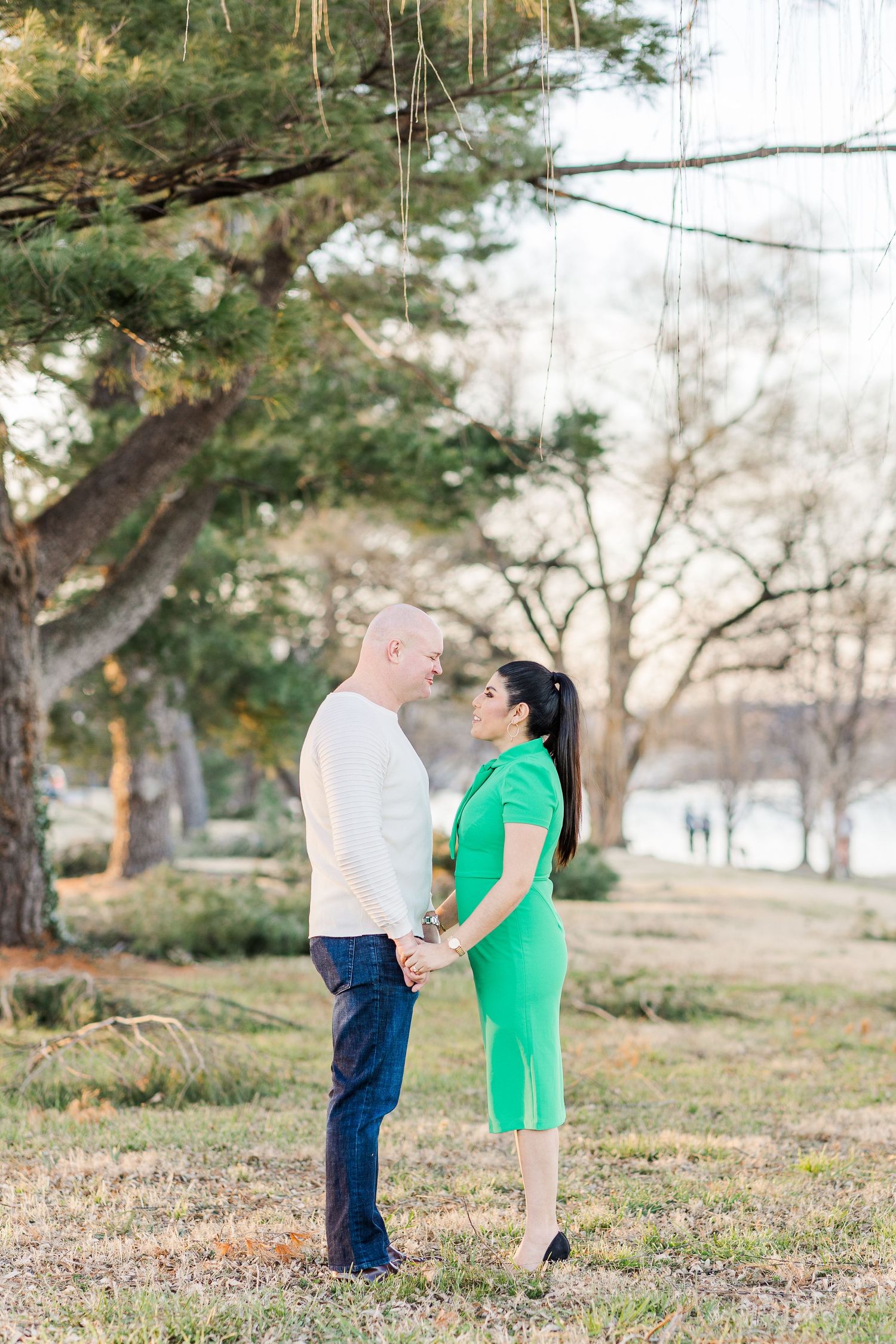 Couple sharing romantic moment in park with pine trees in background.