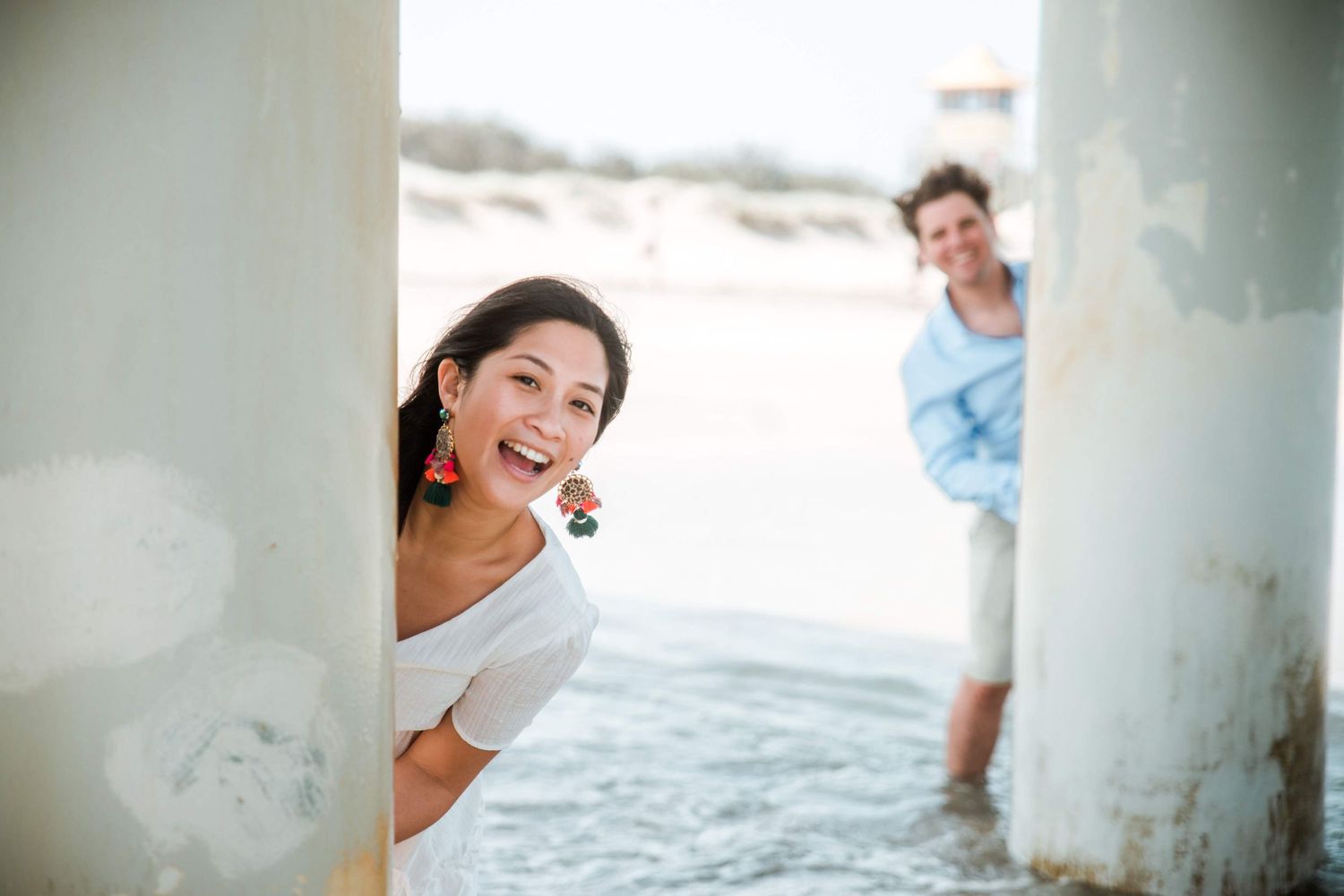 A playful peek-a-boo moment between pillars at the beach with ocean in background.