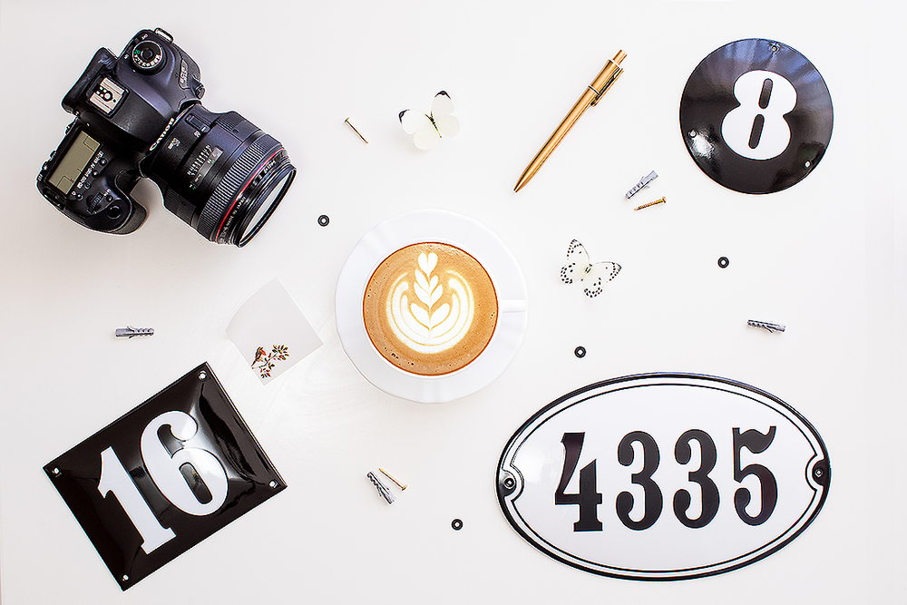 Flat lay photography setup with DSLR camera, latte art coffee, pencil, and number signs including 4335.