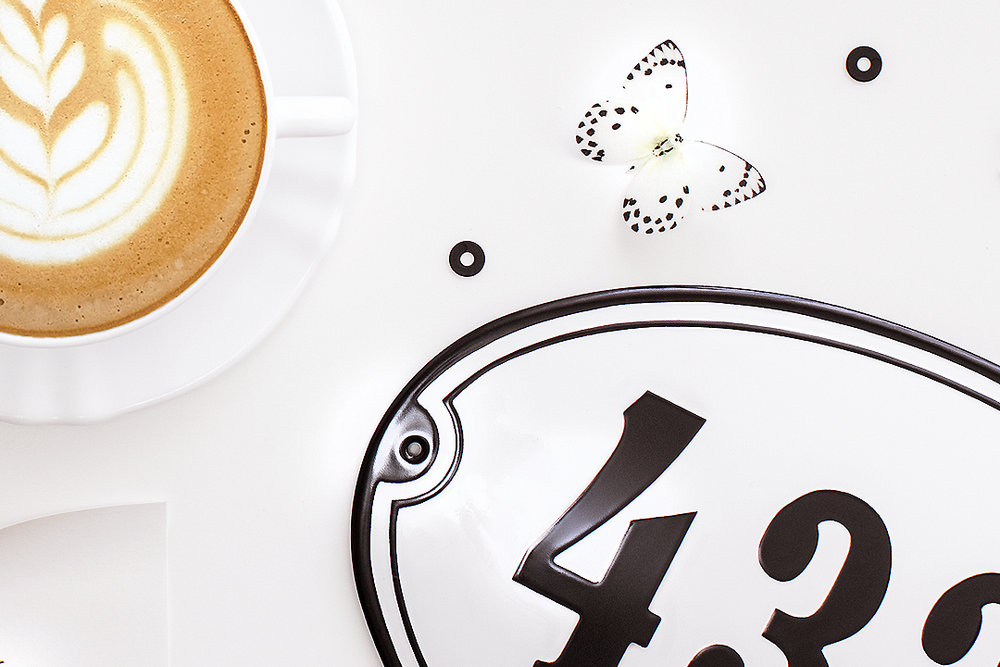 Close-up of latte art coffee cup with decorative butterfly and number plate elements.