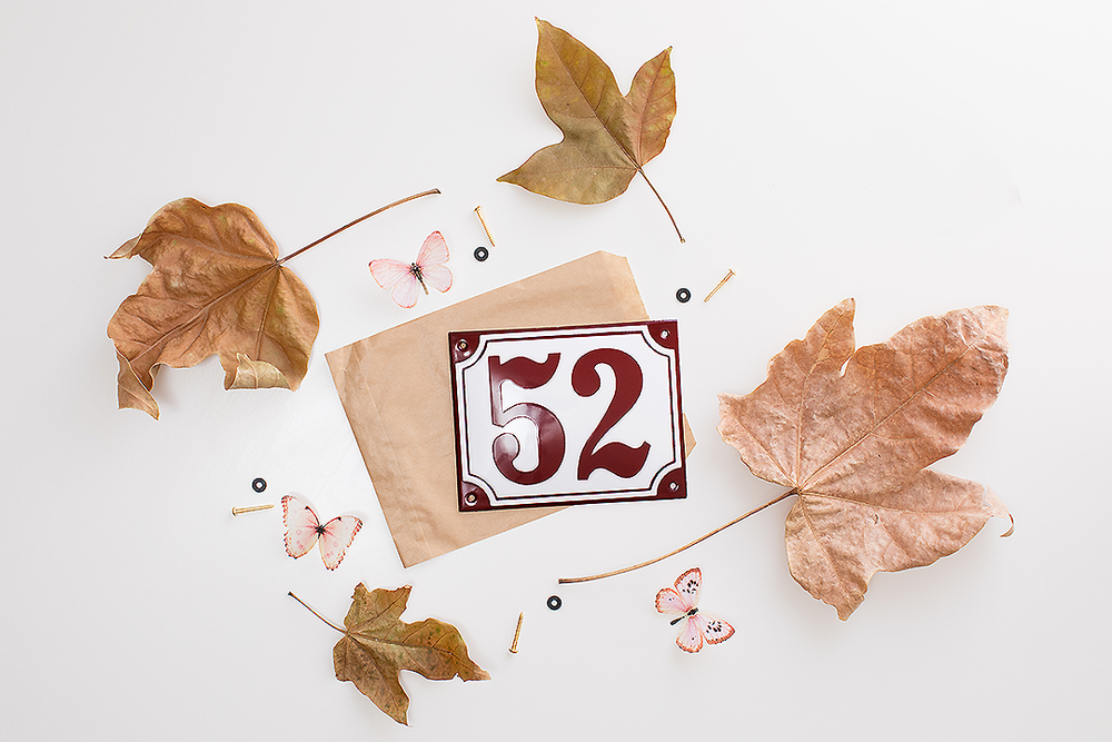 House number 52 plaque surrounded by autumn leaves and butterfly decorations on white background.