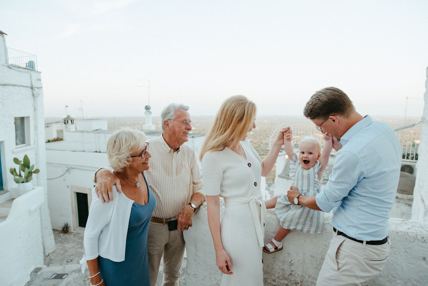 Group enjoying social gathering on white rooftop terrace in Mediterranean setting.