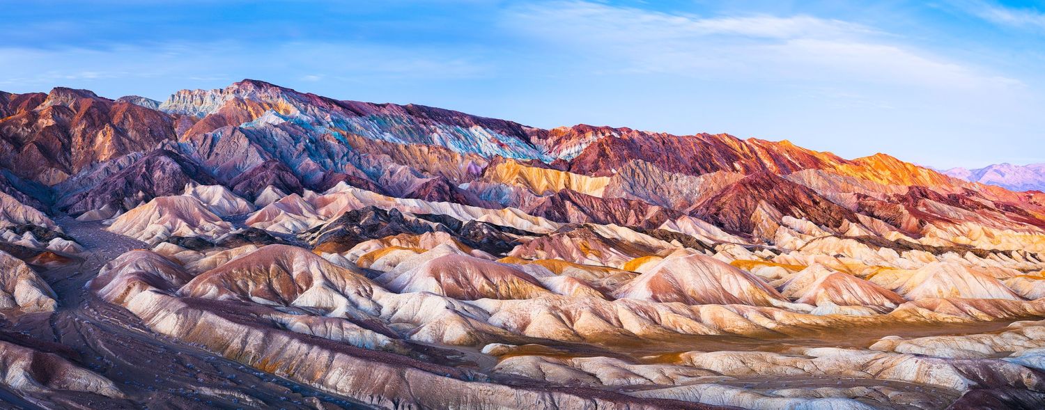 Colorful rock formations stretch across a desert mountain range under blue skies.