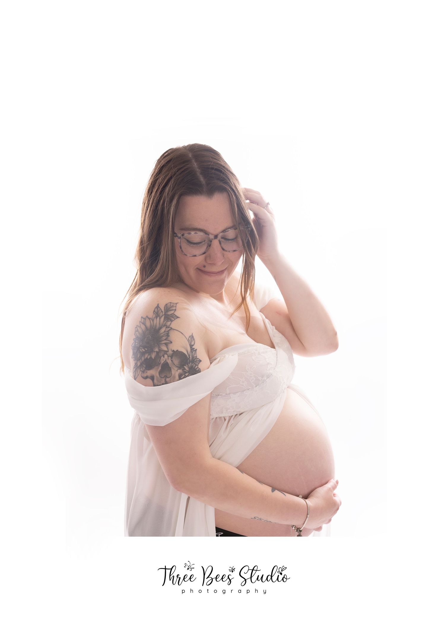 Backlit maternity portrait featuring expecting mother in white dress with visible tattoo.