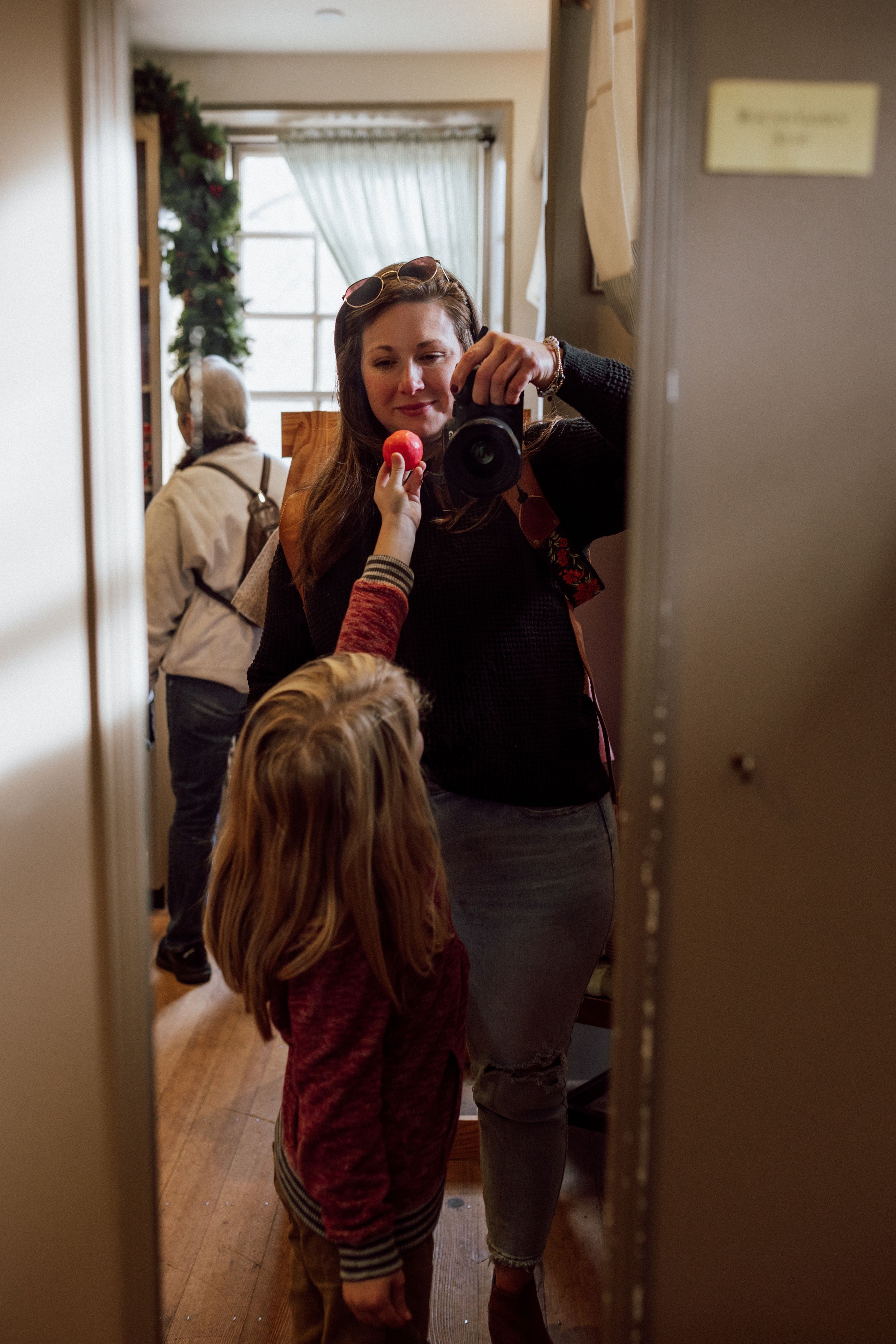 woman in the mirror with camera with child handing her an object in colonial williamsburg store