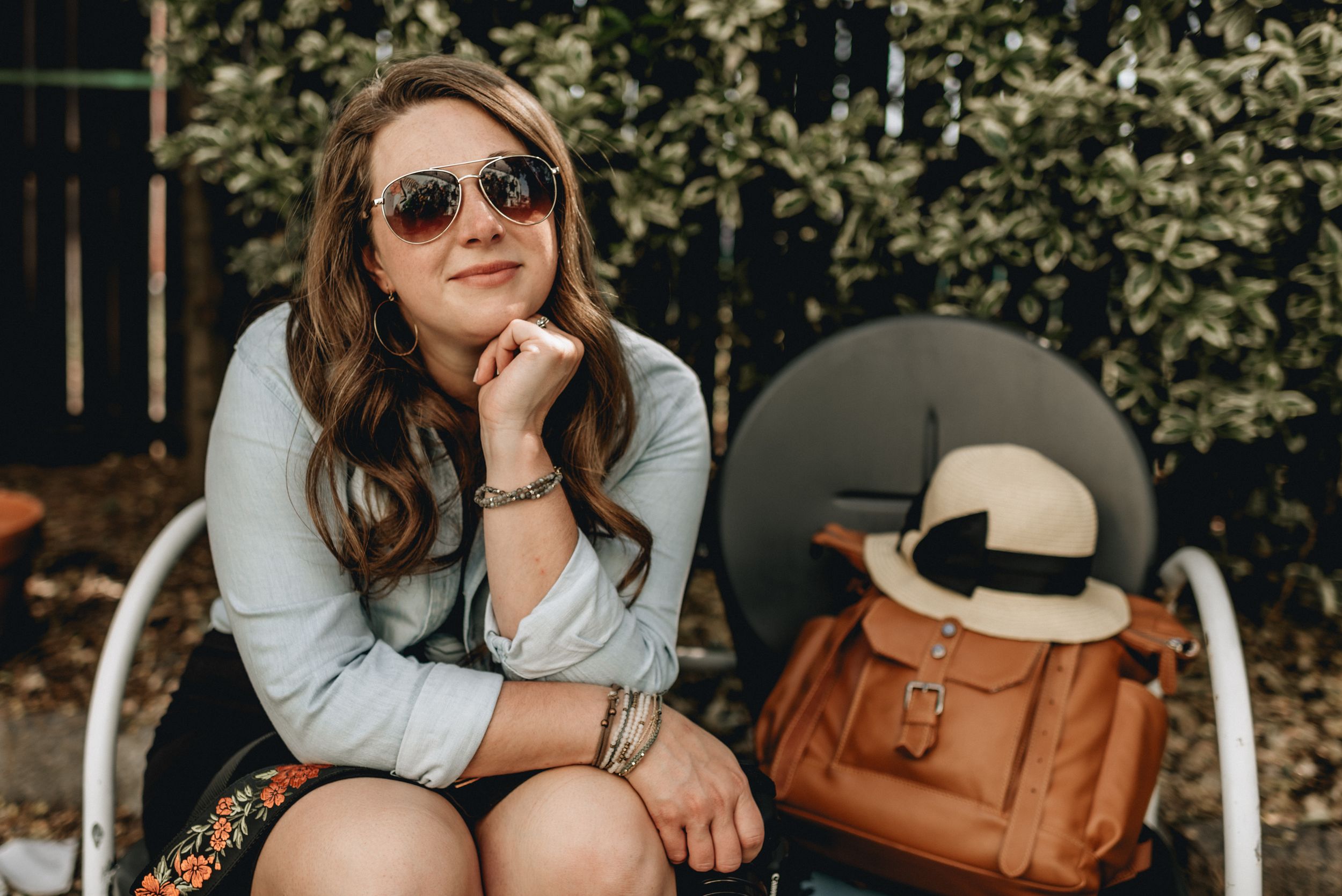 photographer jessica hubbard on a bench with camera bag and hat in norfolk, virginia