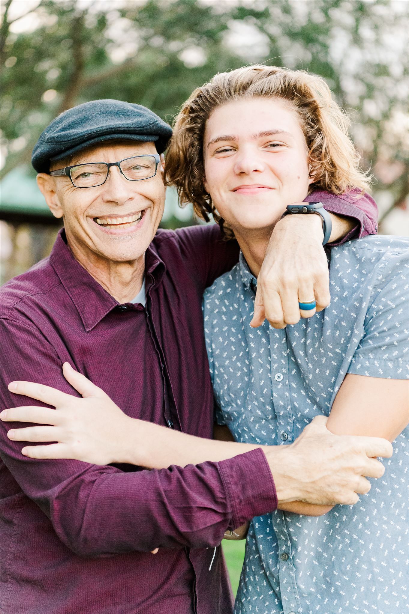 A heartwarming moment of embrace between an older person wearing a flat cap and a younger person in a blue patterned shirt.