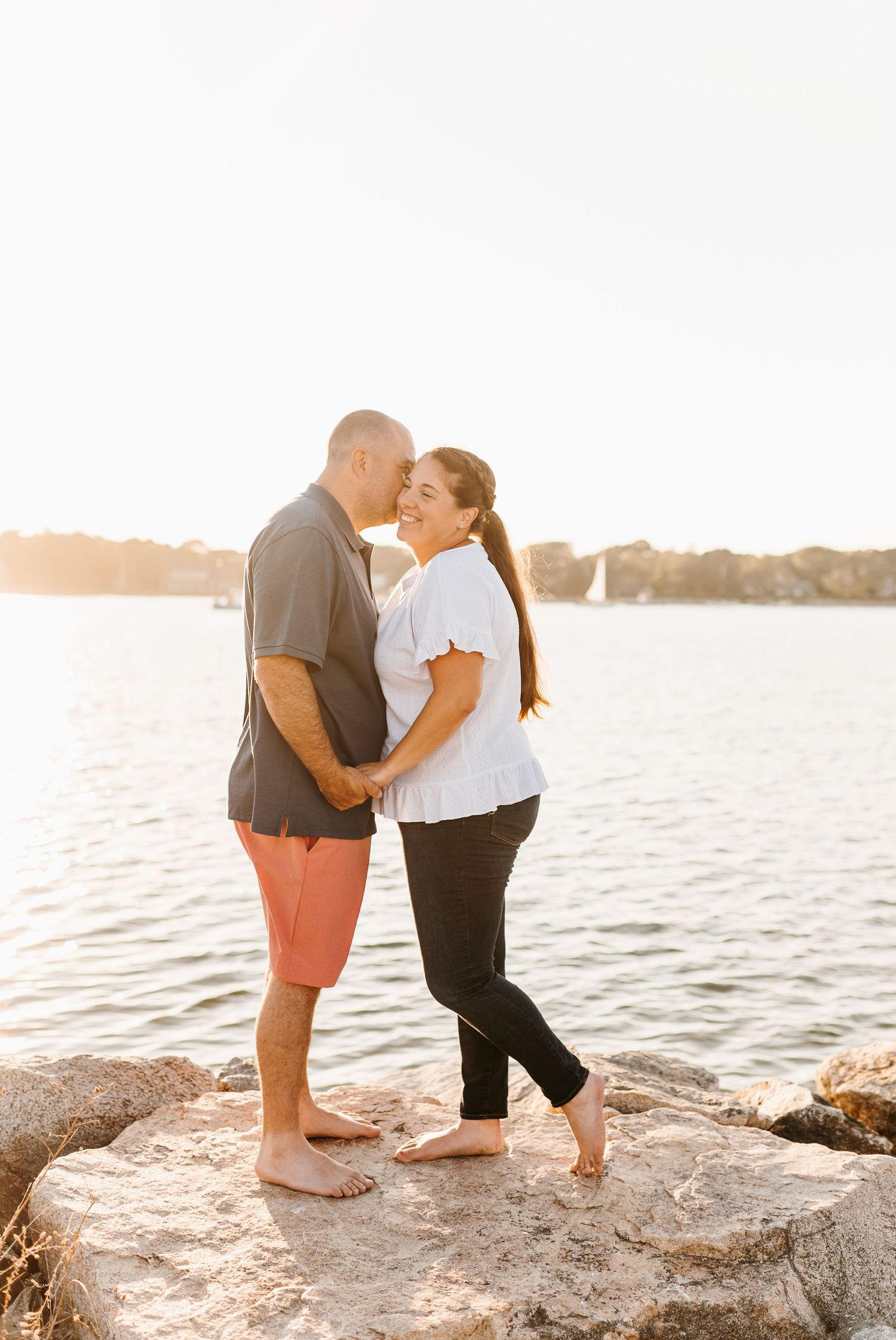 Romantic couple sharing an intimate moment on rocky waterfront during golden sunset.