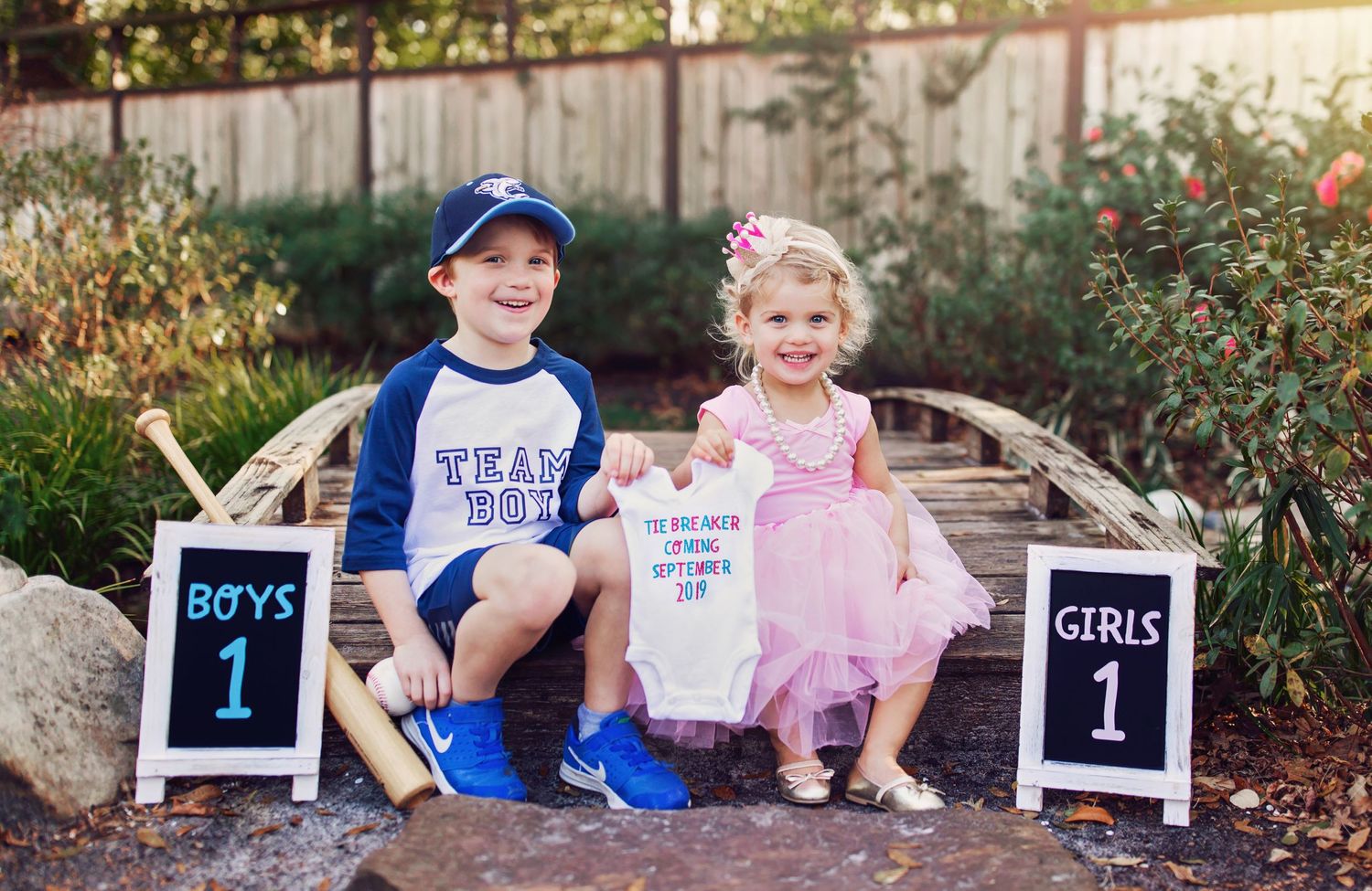 Two children sit on wooden bench with baseball and ballet themed signs for portraits.