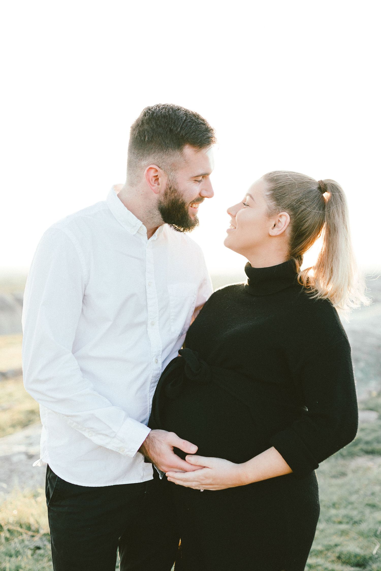 Intimate couple in white and black outfits share a loving moment on a rocky landscape at sunset.
