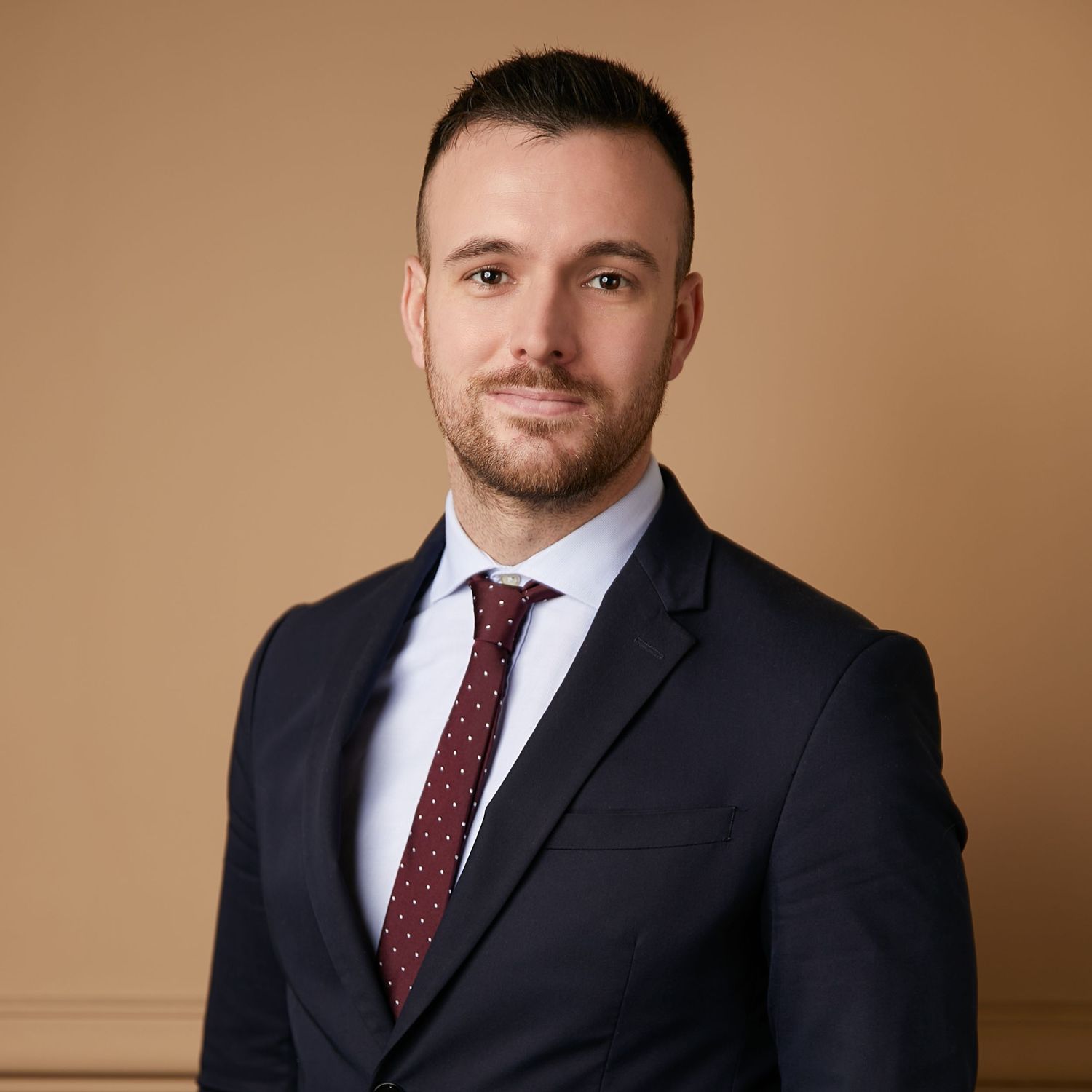 Professional portrait of a person in business suit with red tie against brown background.