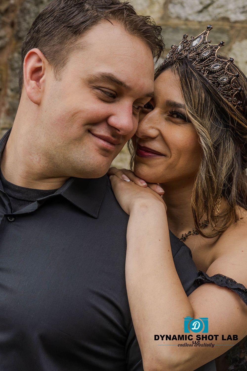 A romantic close-up portrait of a couple sharing an intimate moment against a stone wall background.