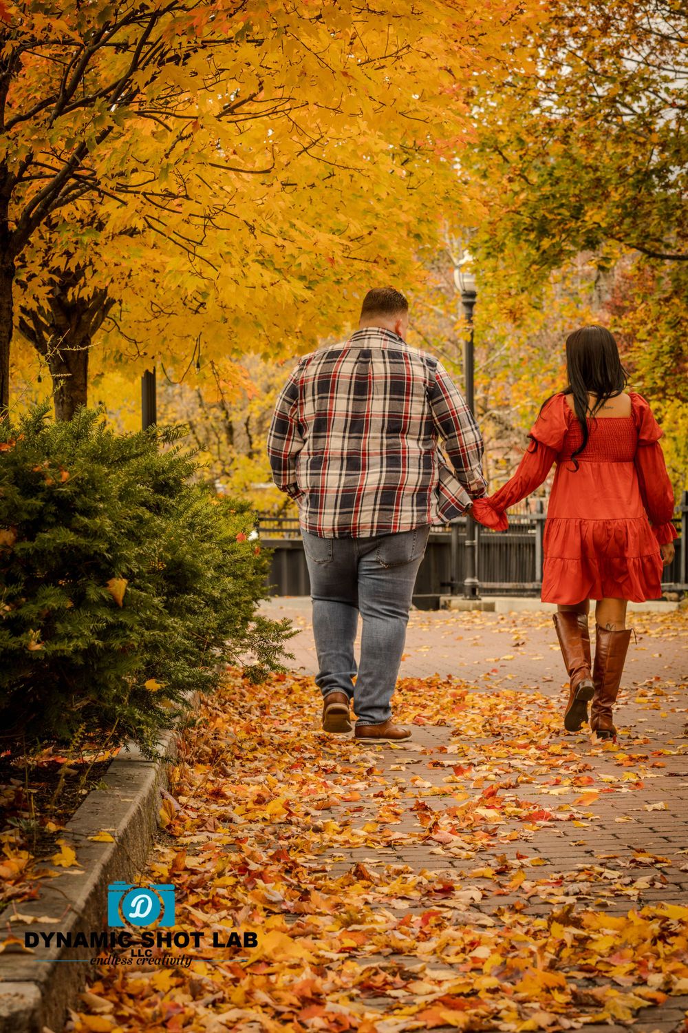 A couple walks hand in hand along a path covered in vibrant yellow fall leaves.