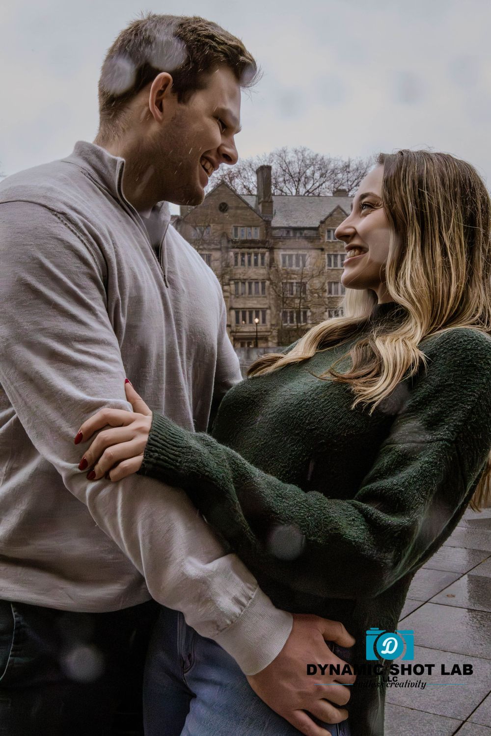 A couple embraces and laughs together while wearing cozy sweaters on an overcast day.