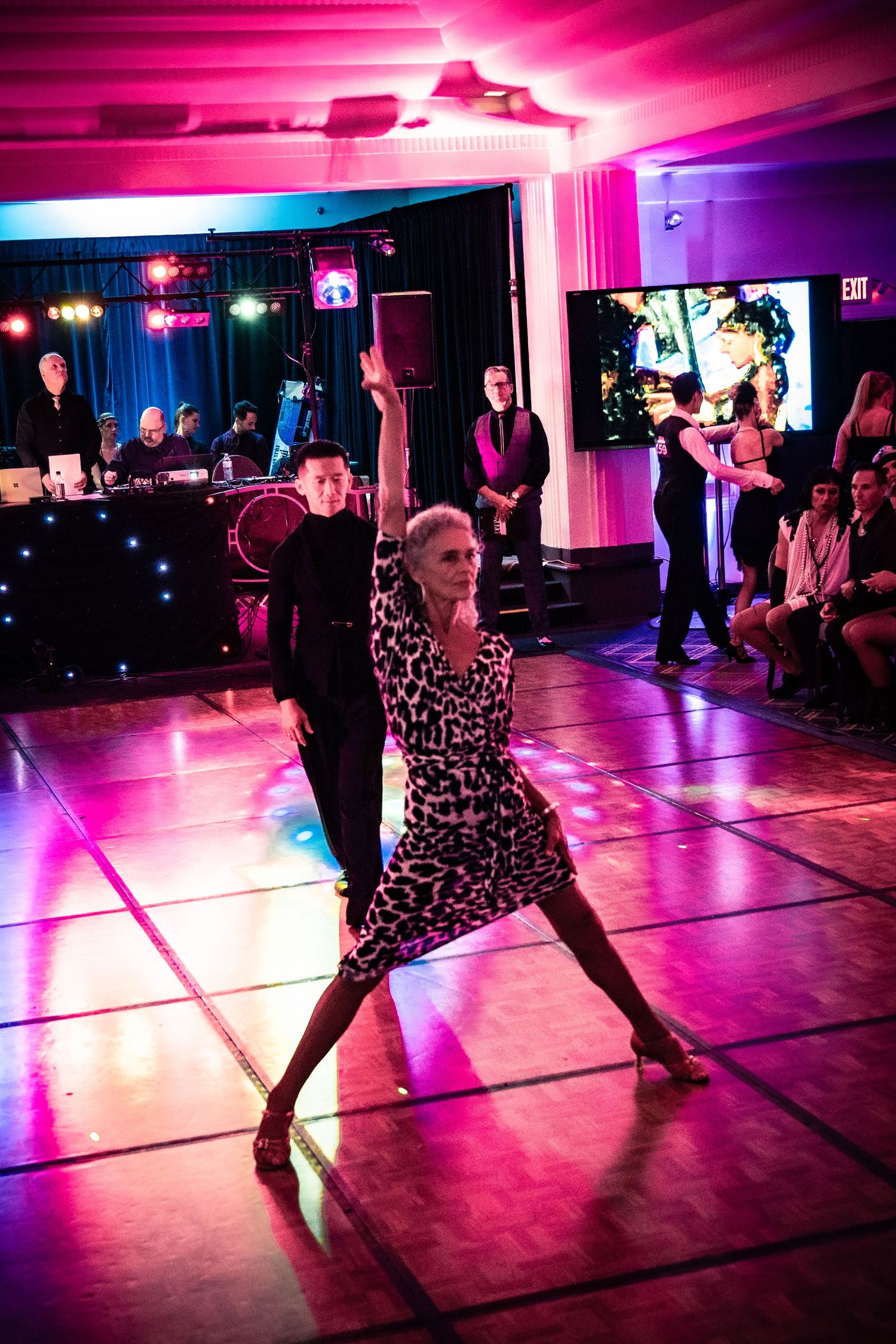 Couple performing elegant ballroom dance on illuminated floor with pink lighting at formal dance competition.