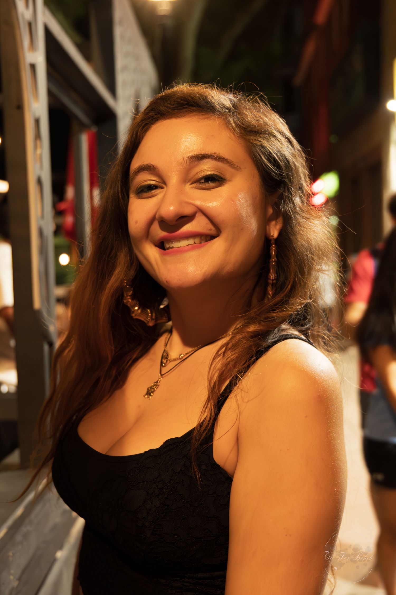 Smiling young woman with long brown hair wearing a black top at an outdoor nighttime event.
