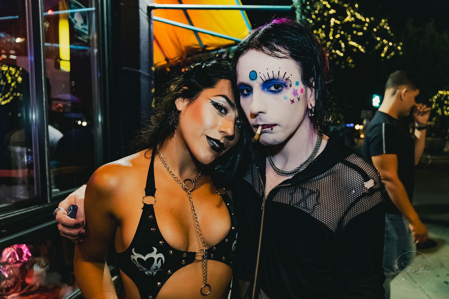 Two people in dramatic Halloween makeup and edgy outfits pose together at a nighttime outdoor event.