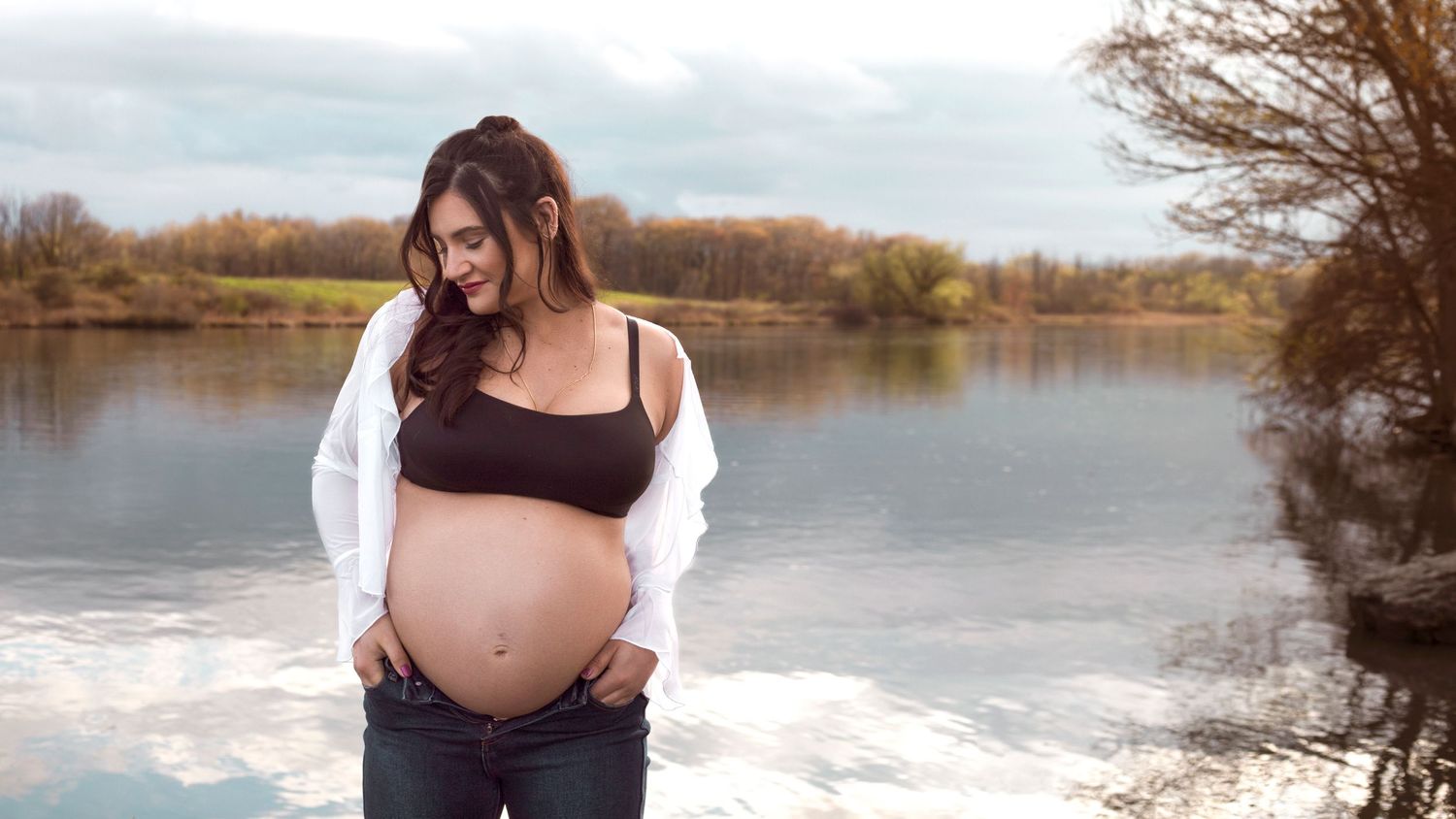 Artistic maternity portrait taken outdoors near a lake during golden hour.