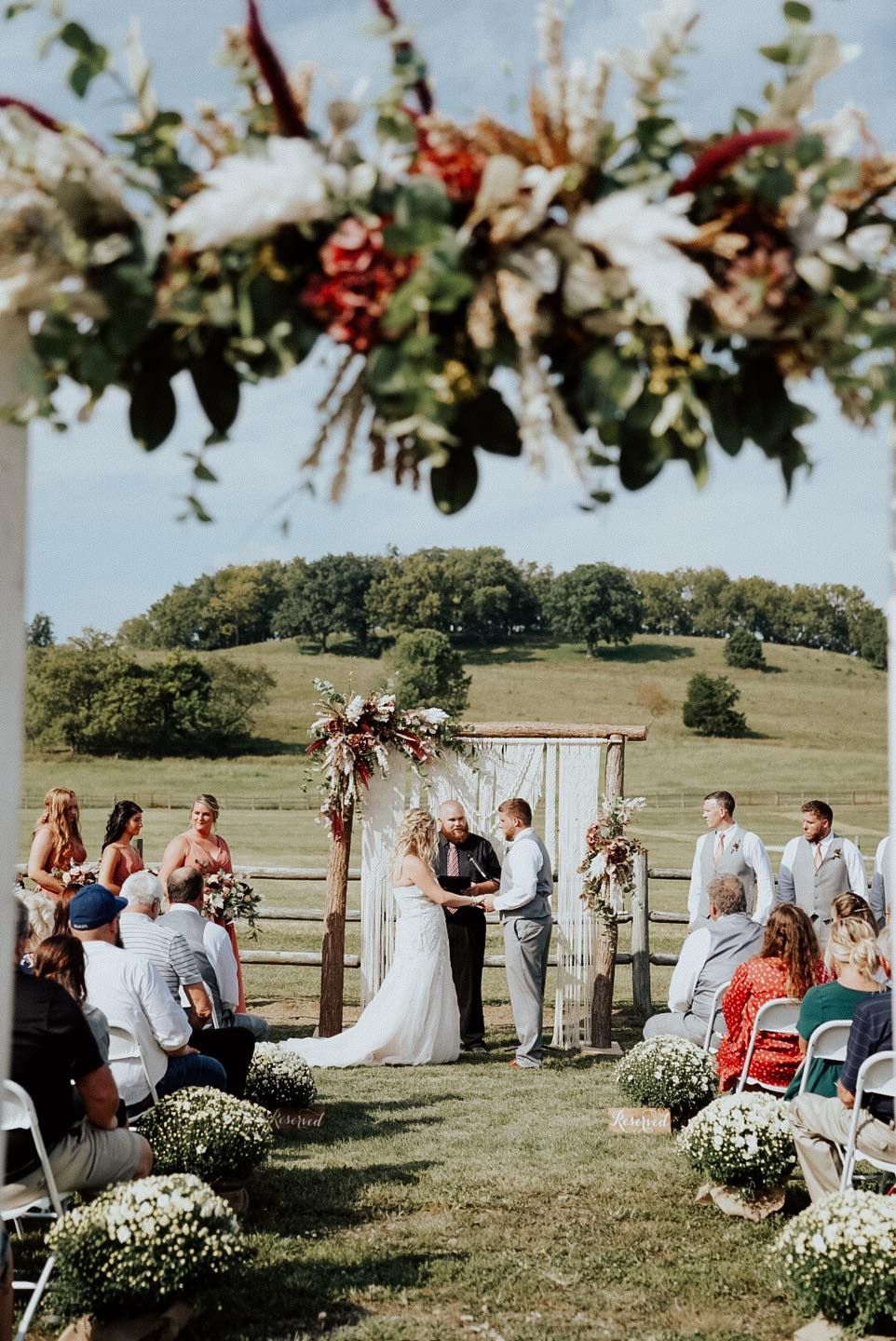 An outdoor wedding ceremony with floral arch decorations and white chairs on a scenic hillside.