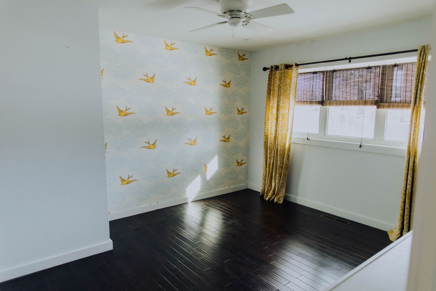 Spacious bedroom with hardwood floors, yellow curtains, and bird-themed wall design.