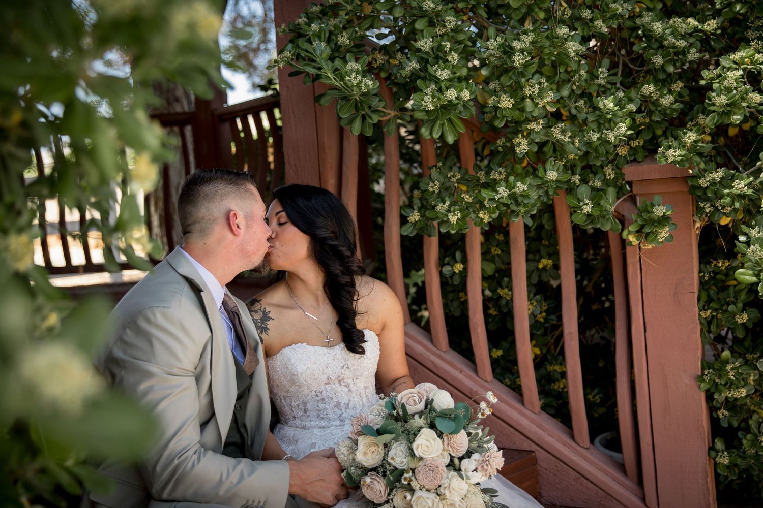 Romantic wedding couple sharing tender moment on rustic wooden stairs with floral bouquet.