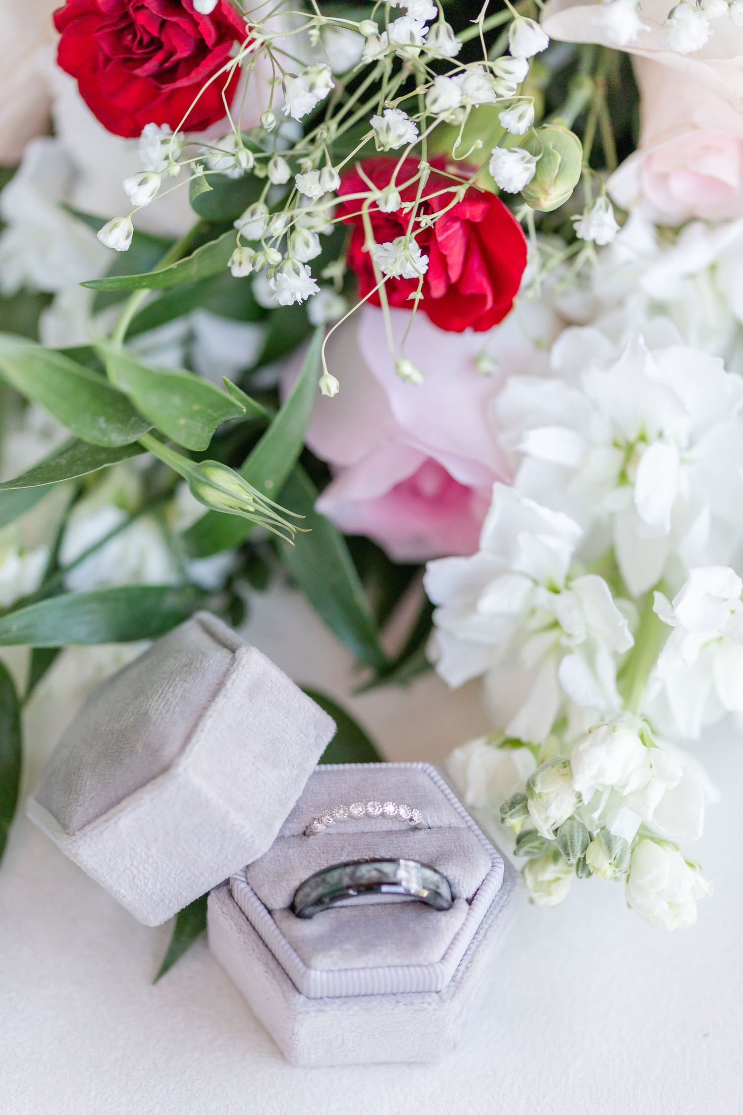 Wedding rings in gray velvet box surrounded by red and white flowers.