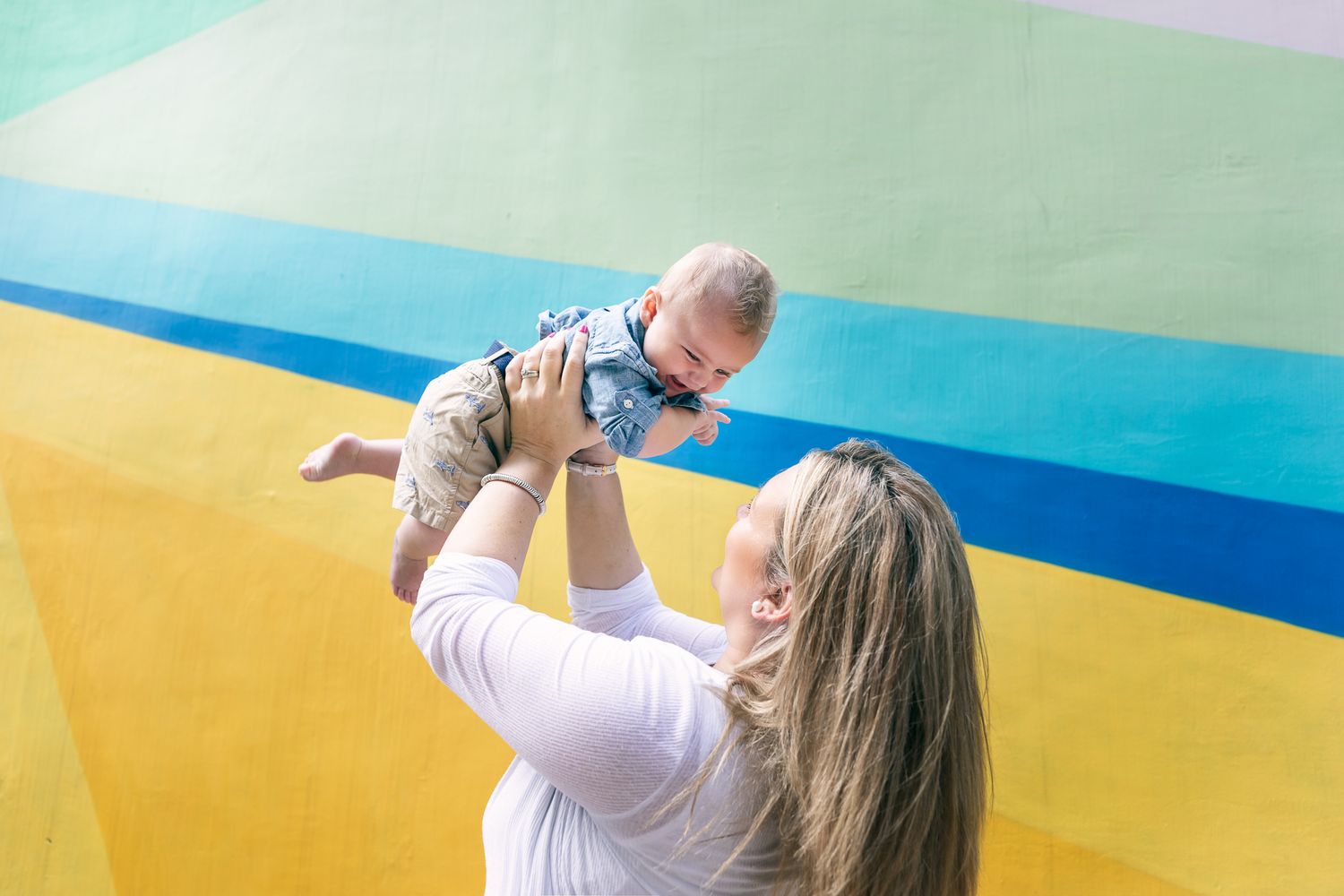 Parent lifting baby in air against colorful geometric background outdoors.