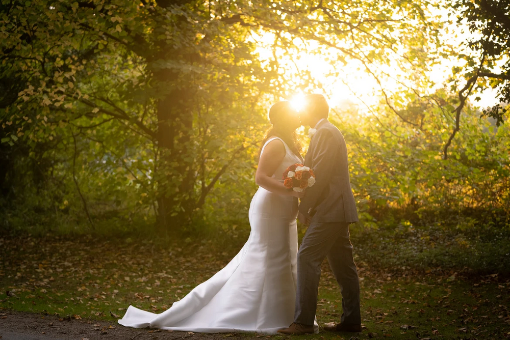 a newly wed couple with a sunlit backdrop kissing with he sub shining creating a silhouette