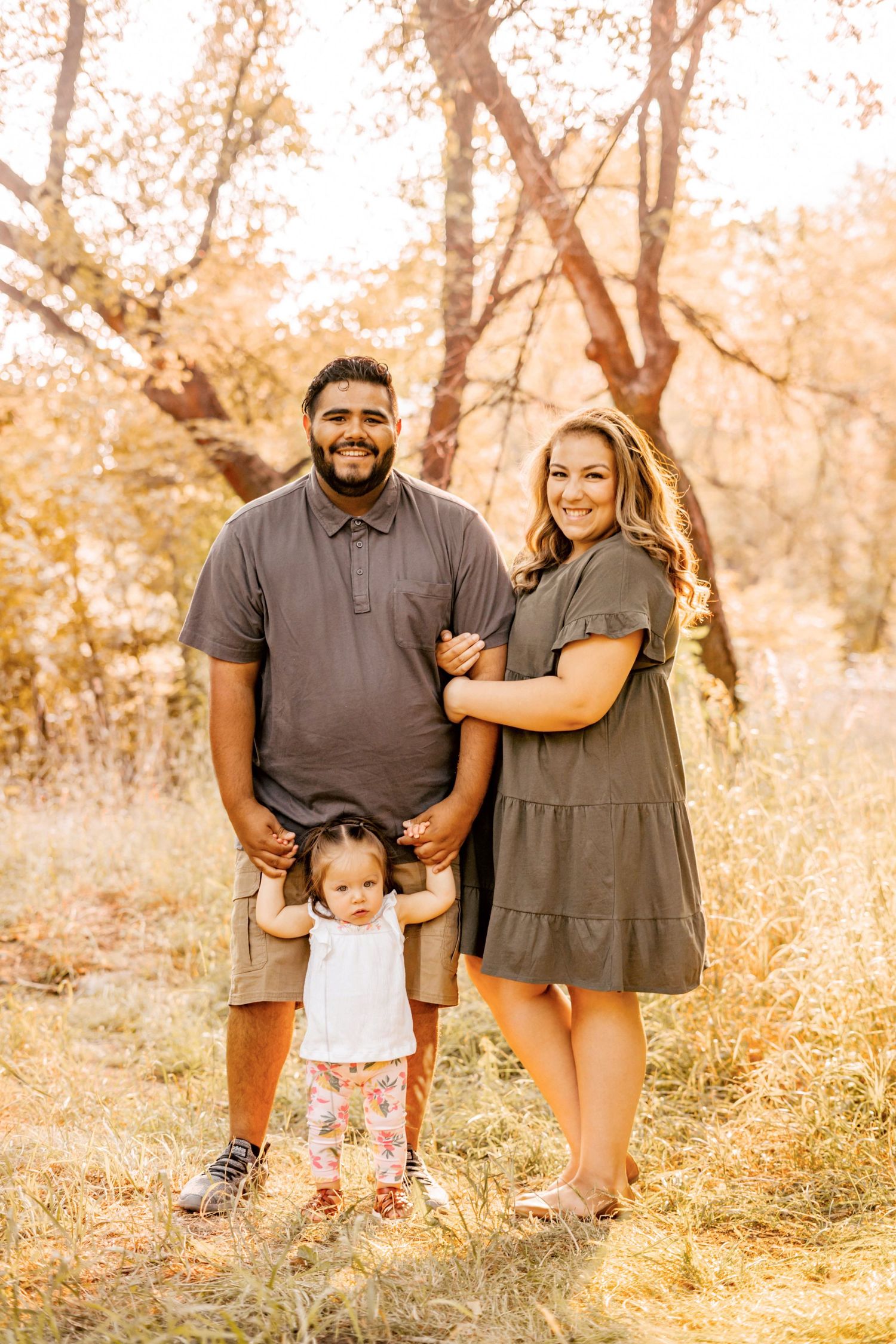 Autumn family portrait with warm lighting and fall foliage in background.