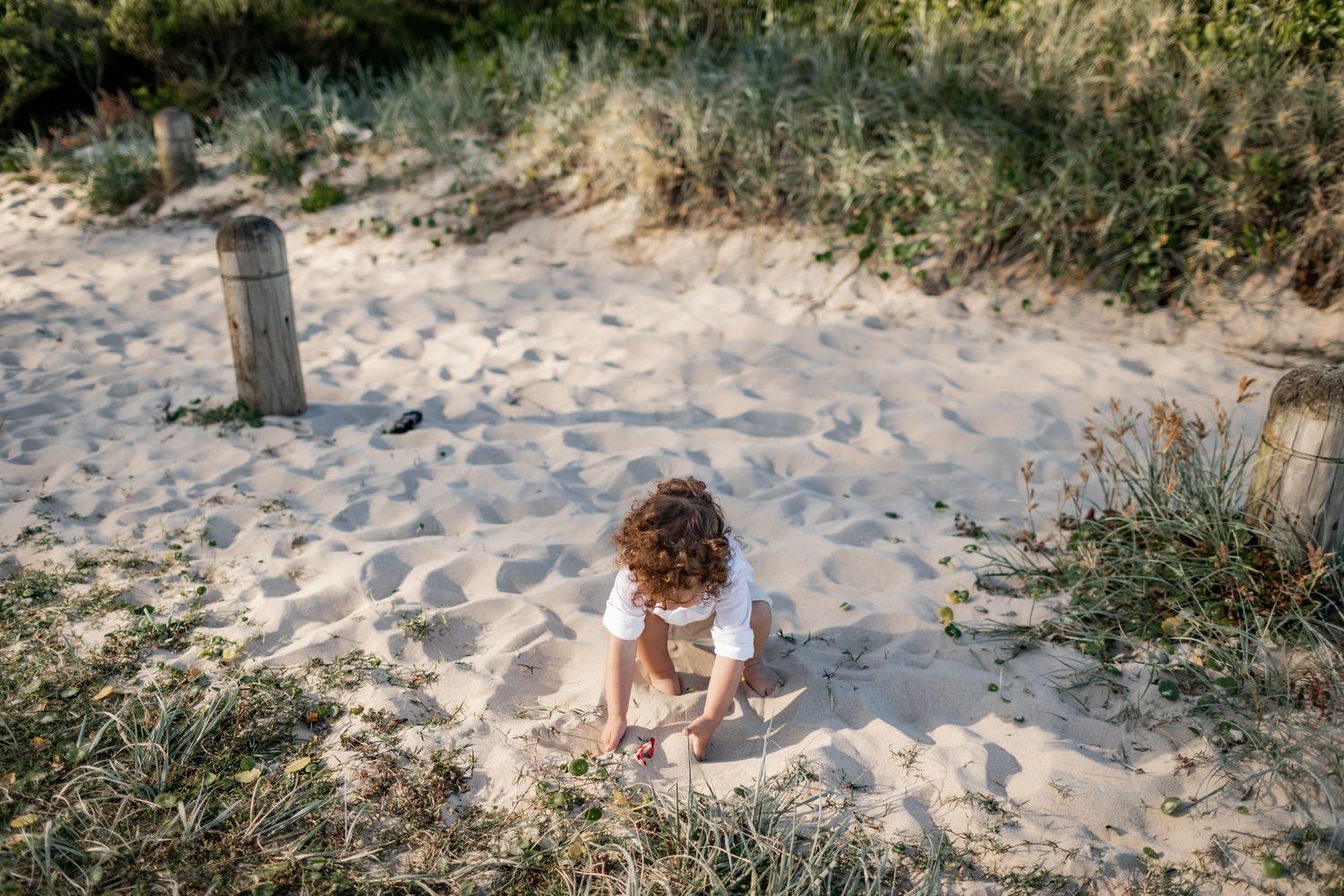 Child playing in the sand on a beach path surrounded by coastal vegetation.